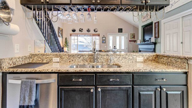 A kitchen with dark wood cabinets, a granite countertop, a stainless steel sink, and a wine rack above the sink. - Denver Townhome in Highlands w/ Spacious Yard! (Denver)