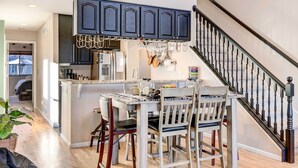 A kitchen with dark blue cabinets, a central island with chairs, and a staircase with black balusters. - Denver Townhome in Highlands w/ Spacious Yard! (Denver)