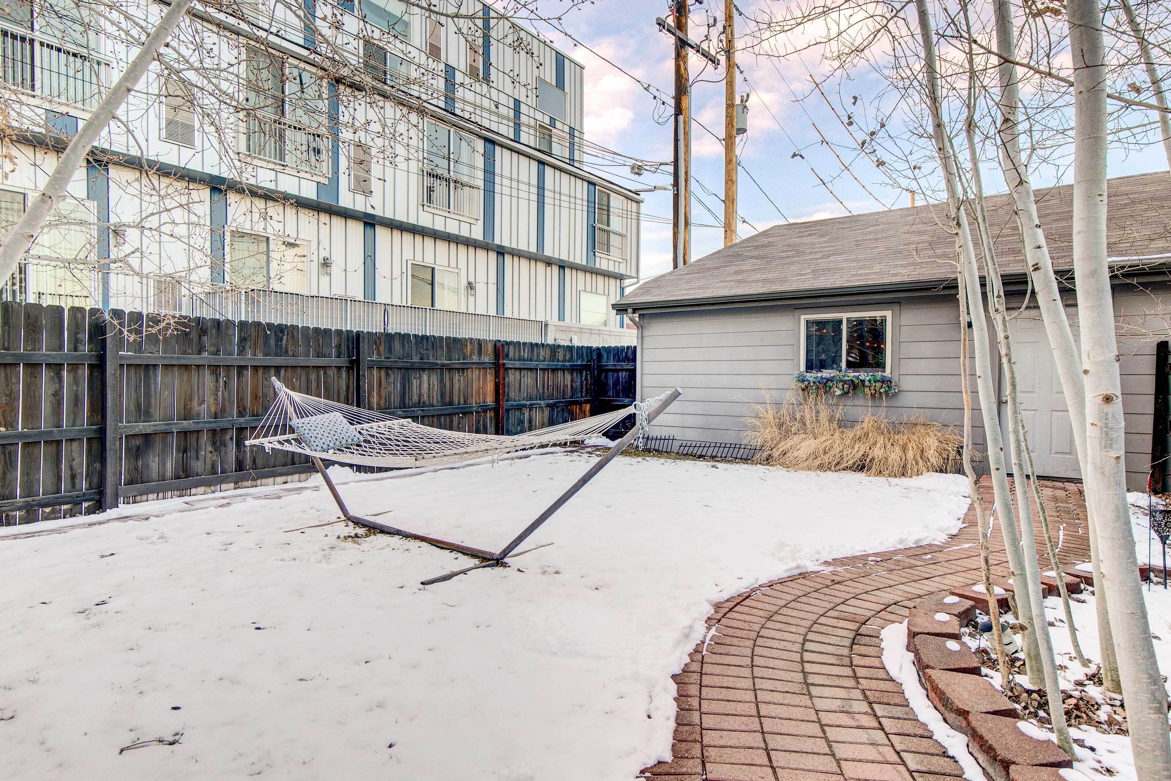 A snow-covered backyard with a hammock, a brick pathway, and a wooden fence.