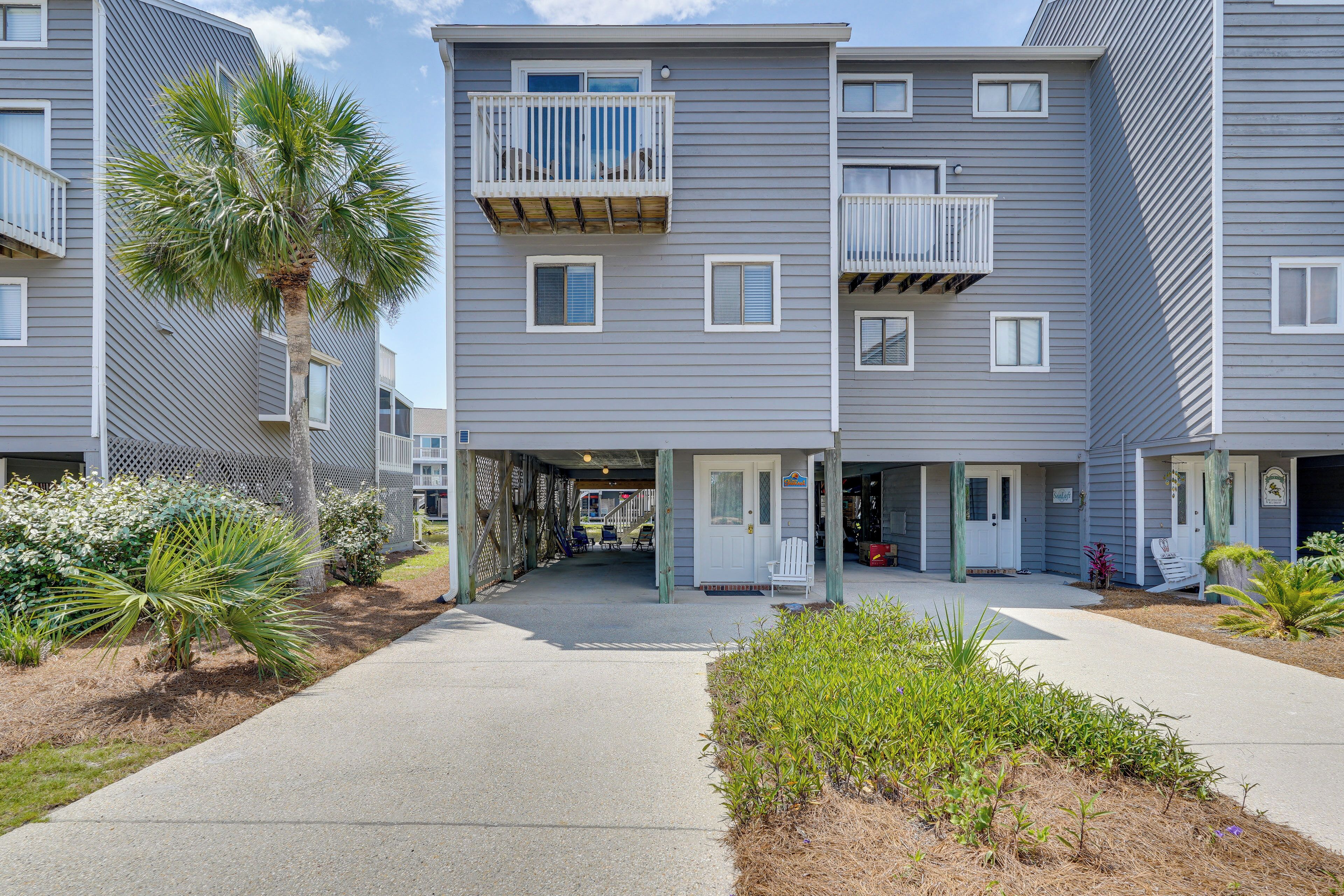A multi-story residential building with balconies, a covered entrance, and a pathway leading to the entrance.