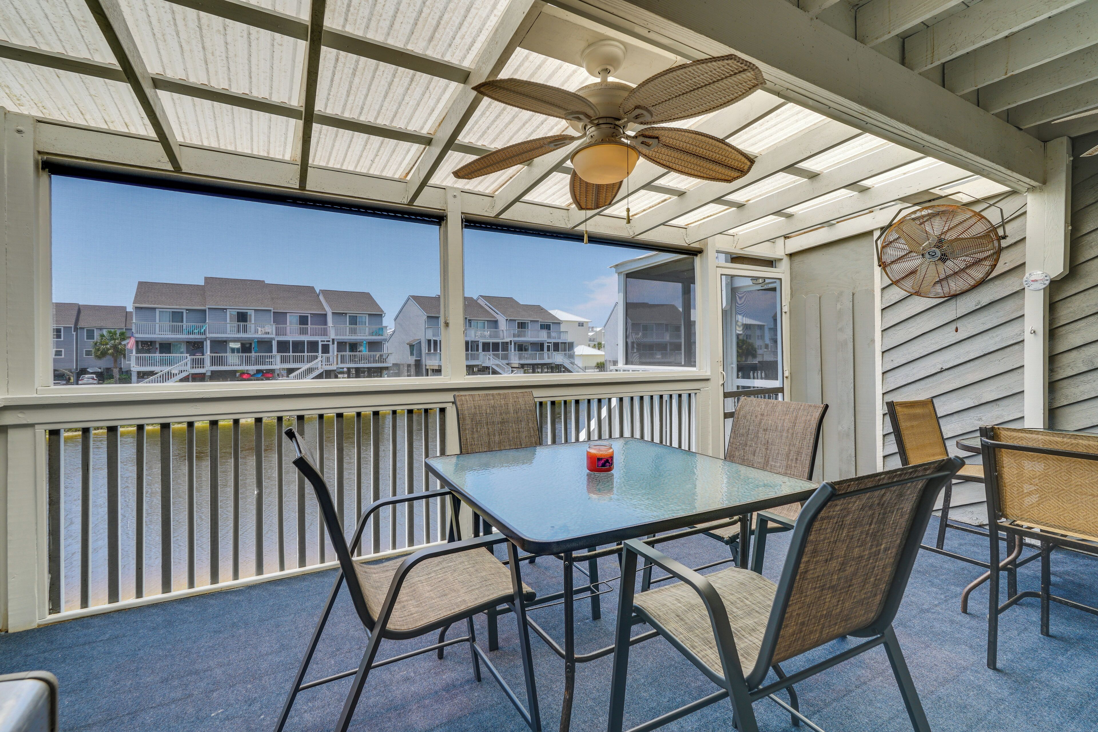 A covered outdoor seating area with a table and chairs, a ceiling fan, and a view of buildings in the background.