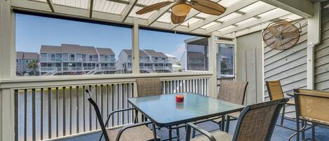 A covered outdoor seating area with a table and chairs, a ceiling fan, and a view of buildings in the background.