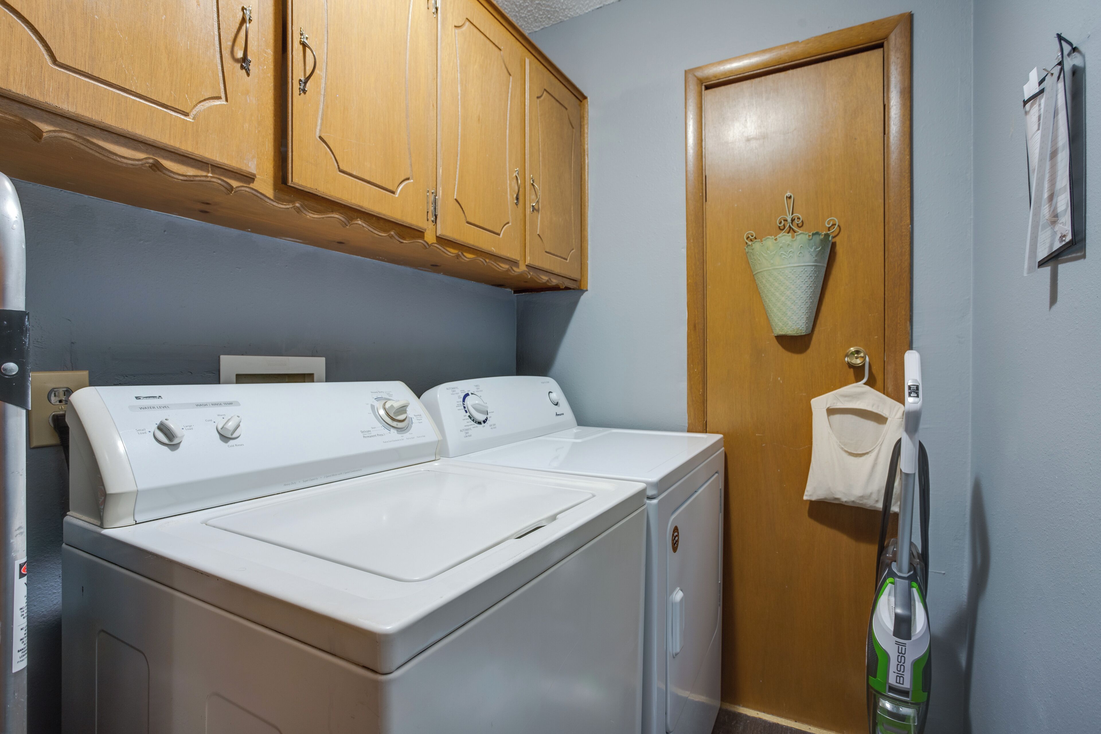 A laundry area with two front-loading washers and dryers, wooden cabinets above, and a door with a towel rack.