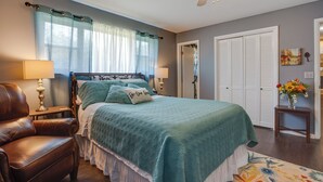 A bedroom with a bed, a chair, a nightstand, a lamp, a ceiling fan, and a door. - Norman Home w/ Yard, Walk to Park & OU Campus! (Norman)