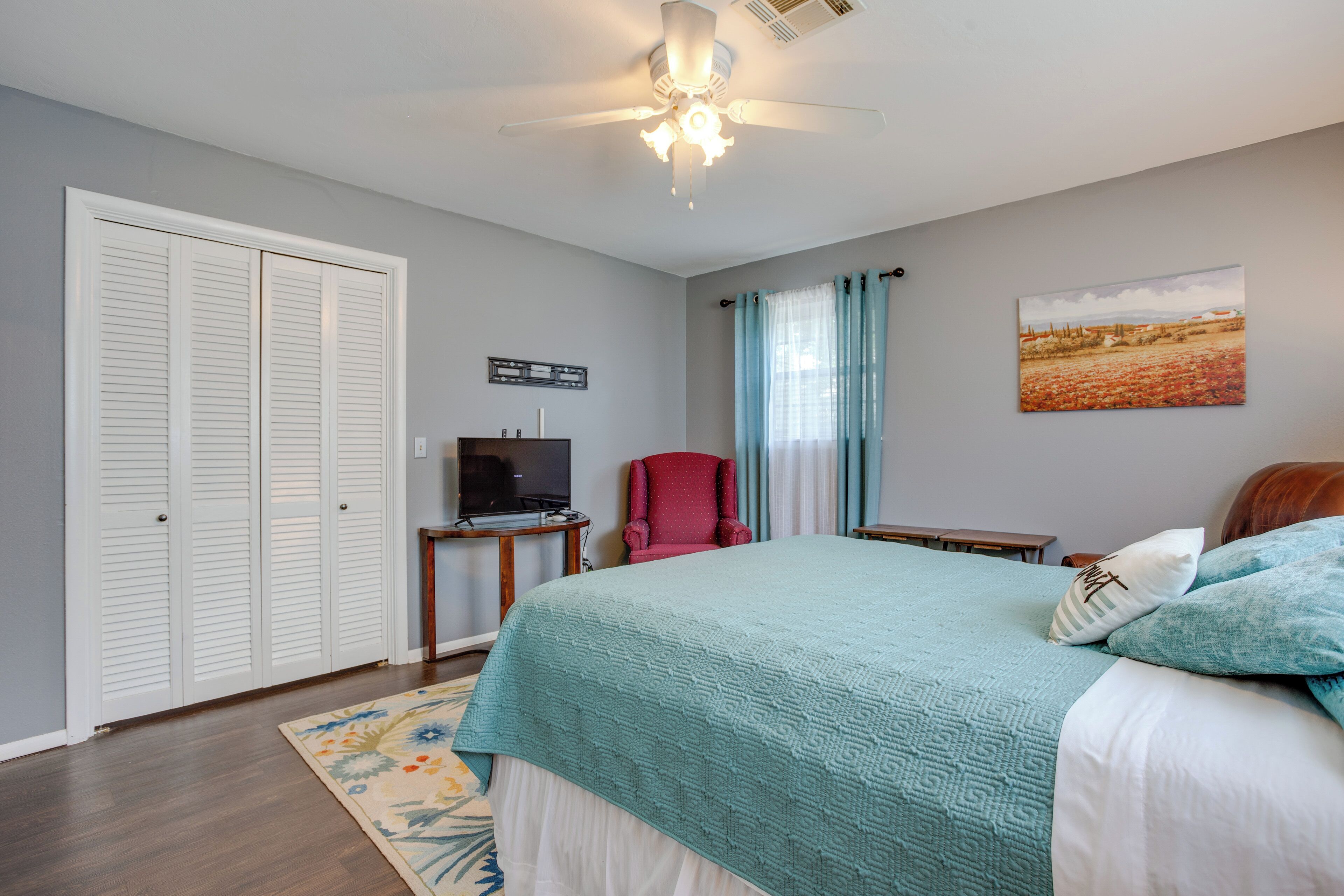 A bedroom with a bed, a television, a red chair, and a painting on the wall.