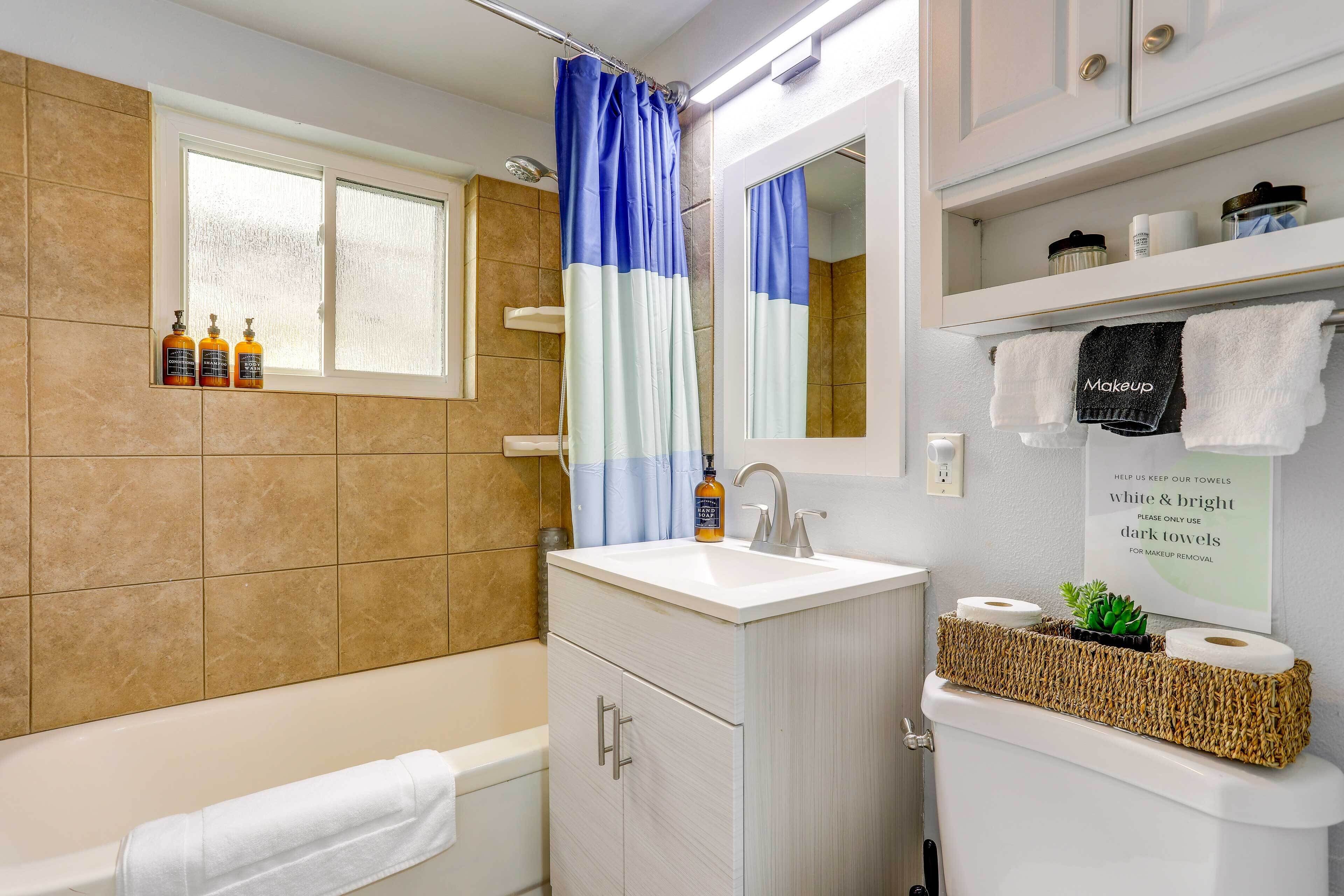 Une salle de bain équipée d’une baignoire, d’un lavabo, d’un miroir et d’un rideau de douche. Des serviettes sont accrochées au mur, et une pancarte demande d’utiliser des serviettes blanches et claires pour enlever le maquillage.
