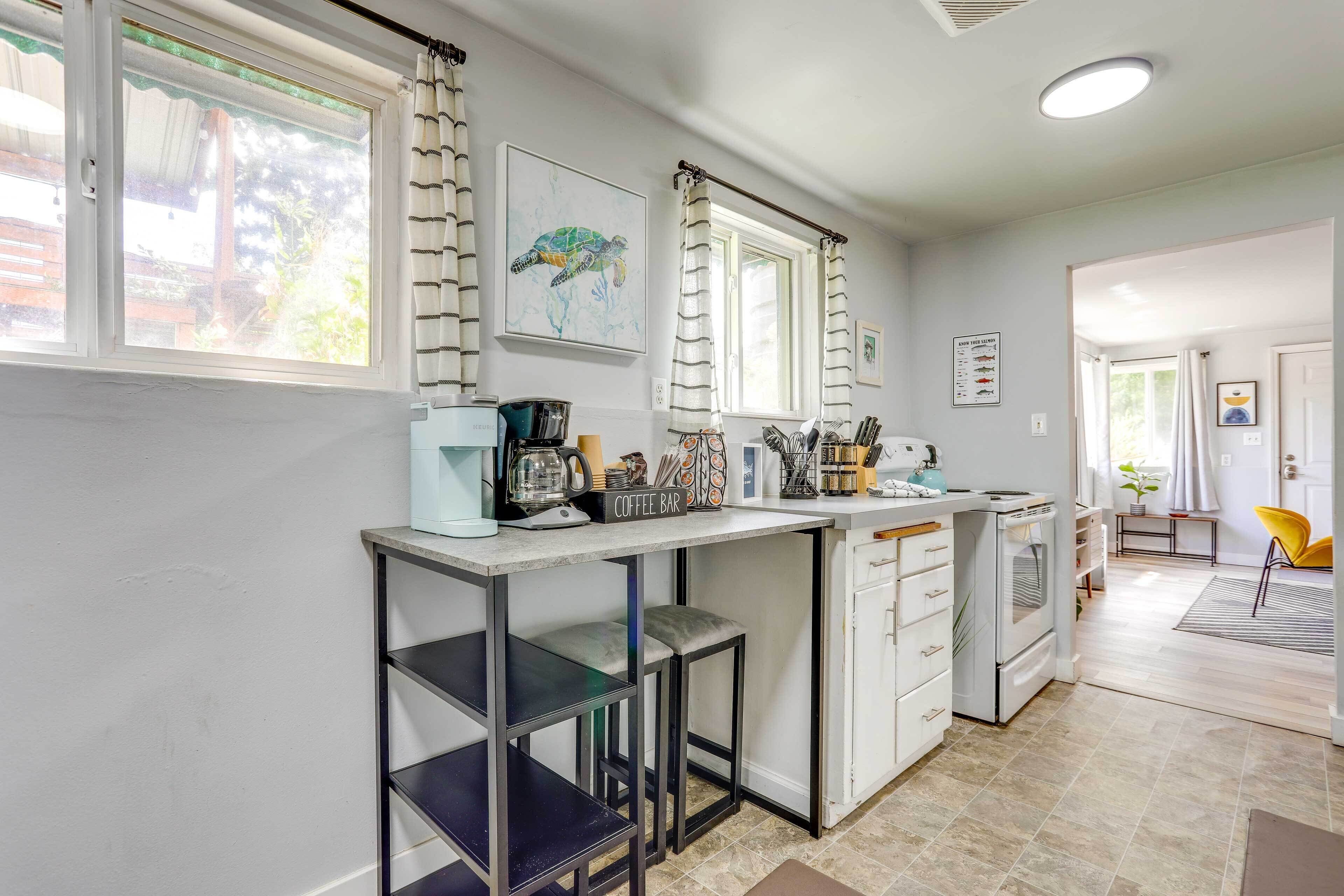 A modern kitchen with a central island, a coffee bar, and a dining area with a yellow chair.