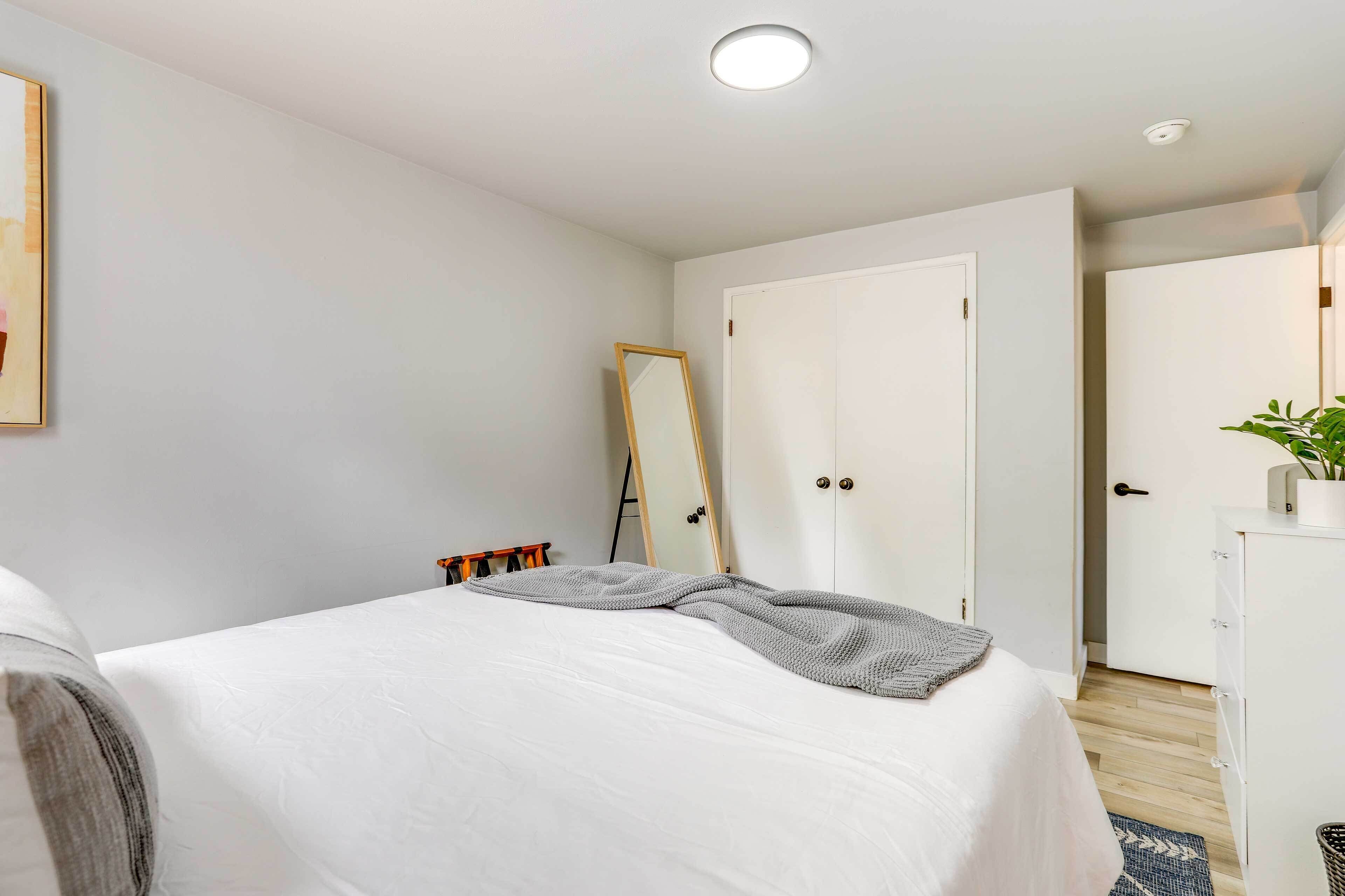 A neatly arranged bedroom with a bed, a wardrobe, a mirror, and a small desk with a plant.