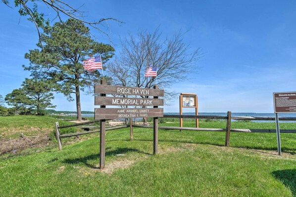 Een houten bord voor Rose Haven Memorial Park met twee Amerikaanse vlaggen, een grasveld en een waterpartij op de achtergrond.