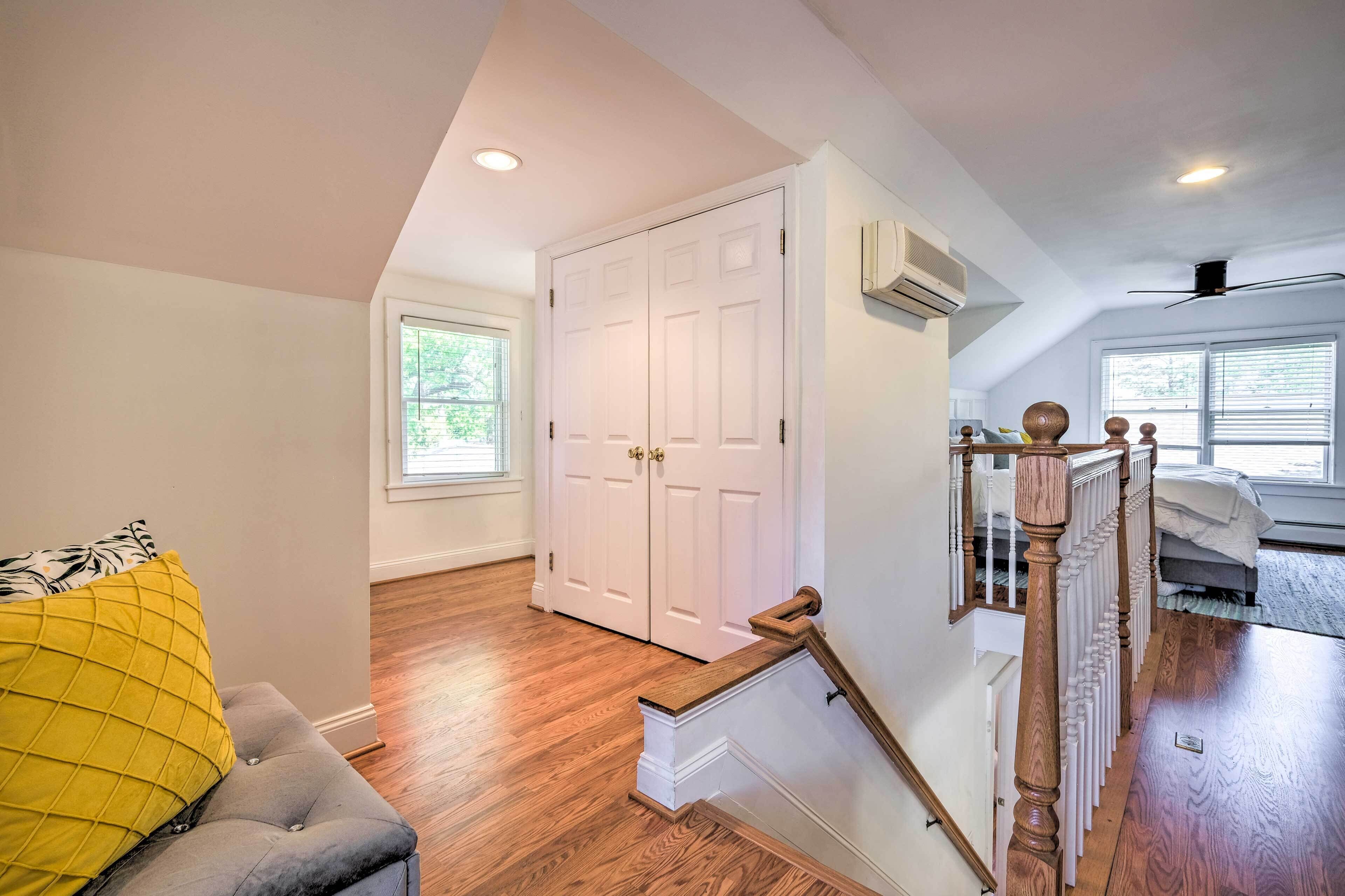 A spacious room with hardwood flooring, a grey upholstered bench, a white door, and a staircase with a wooden railing.