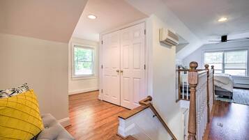 A spacious room with hardwood flooring, a grey upholstered bench, a white door, and a staircase with a wooden railing.