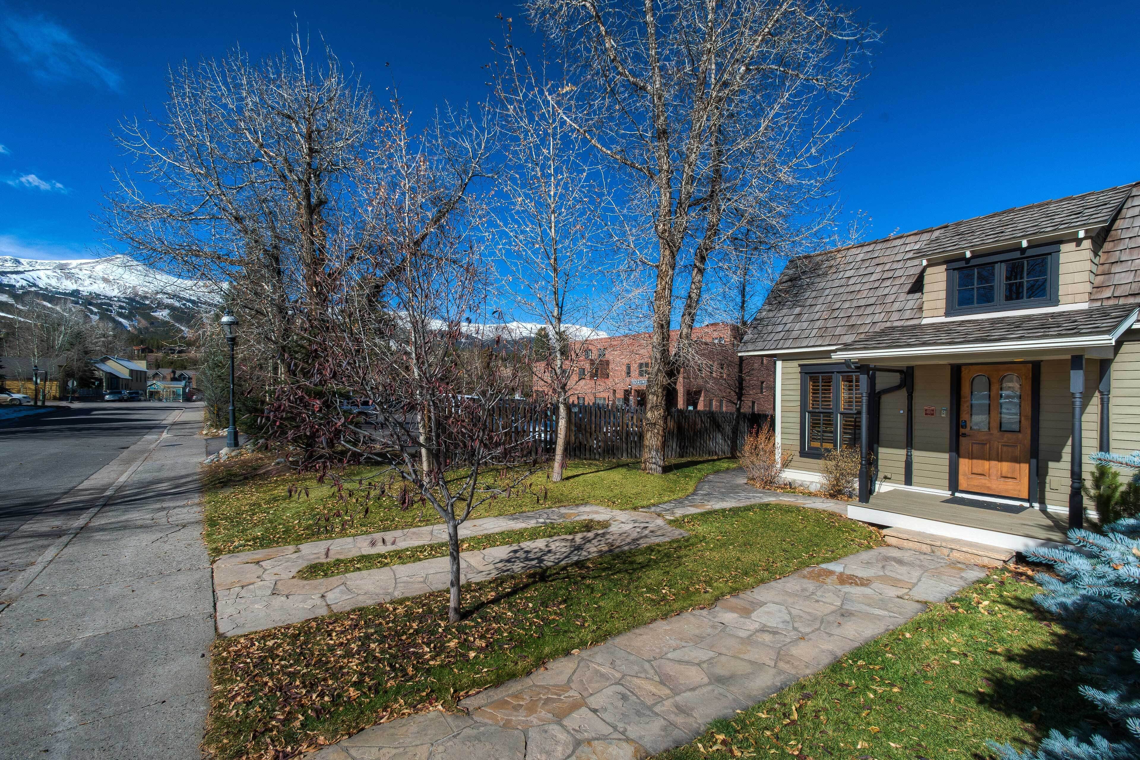 A residential house with a stone pathway leading to the front door, surrounded by a small lawn and leaf-covered ground.