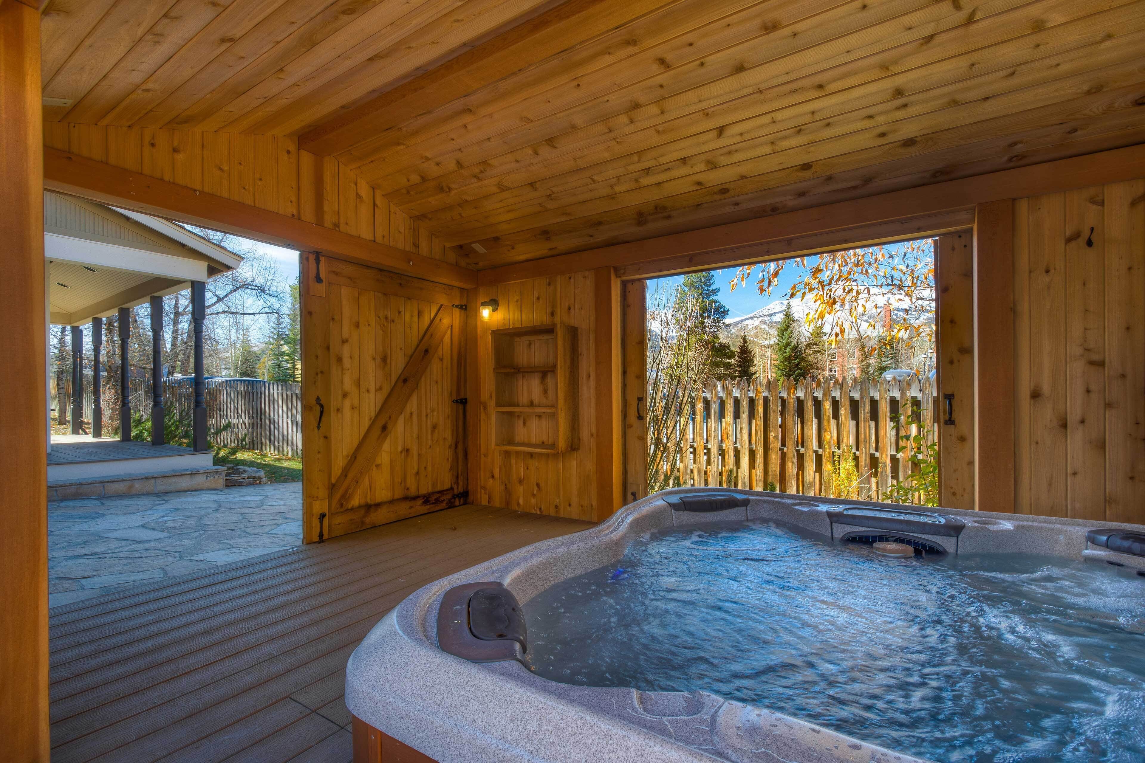 Uma cabana de madeira com hidromassagem, um deck de madeira e vista para uma montanha.