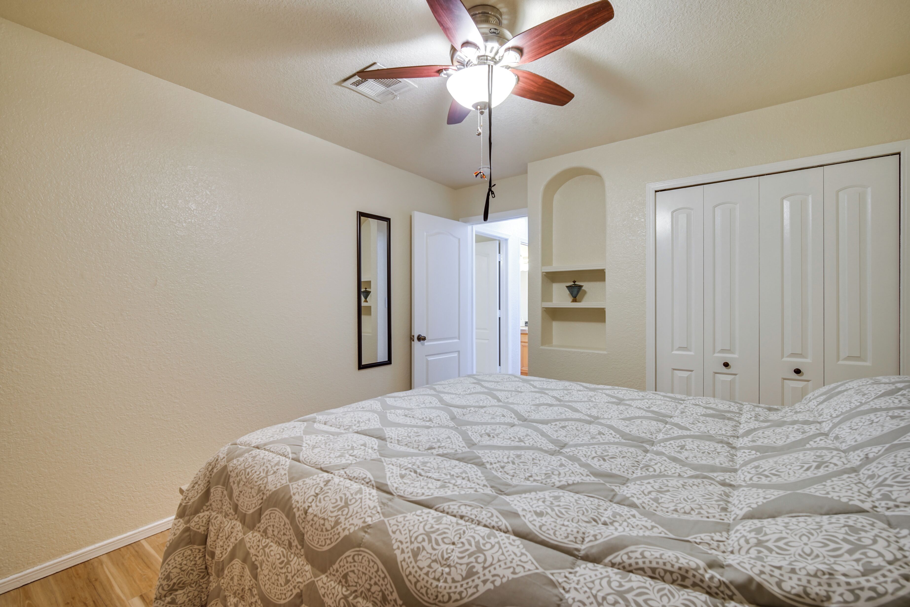Une chambre à coucher avec un lit, un ventilateur de plafond, une porte et une armoire blanche.