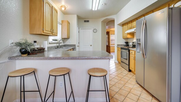 Una cocina con una isla grande, armarios de madera, electrodomésticos de acero inoxidable y piso de baldosas.