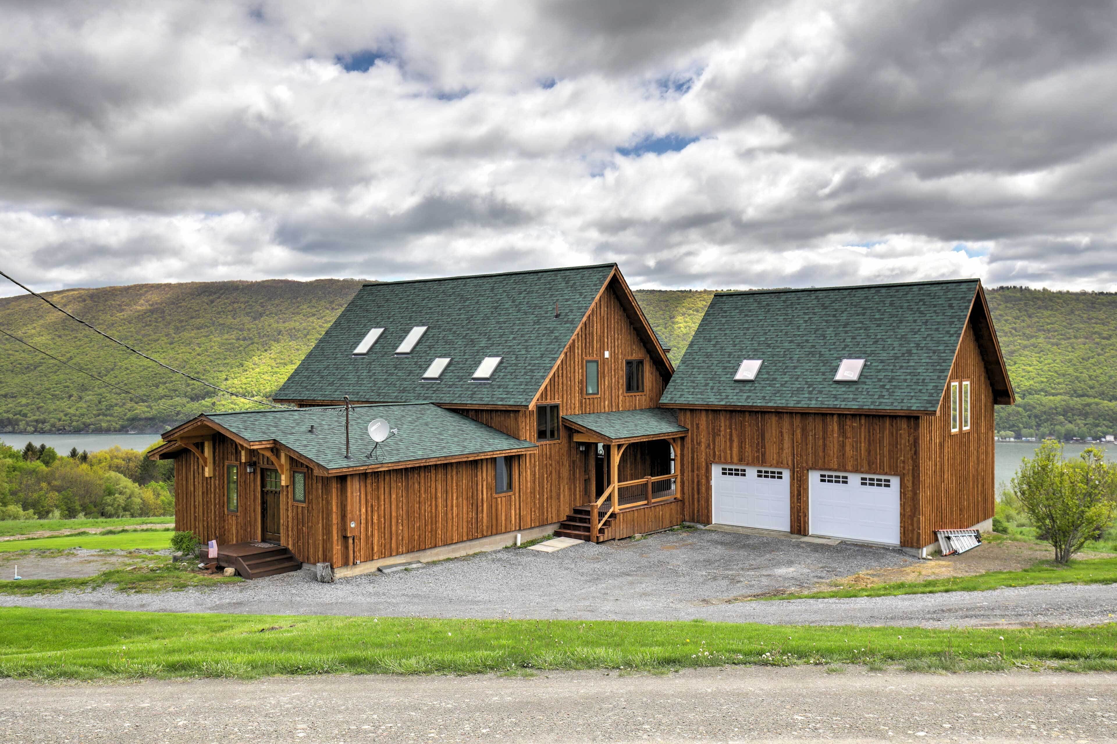 A wooden cabin with two garage doors, a porch, and a view of a lake and hills.