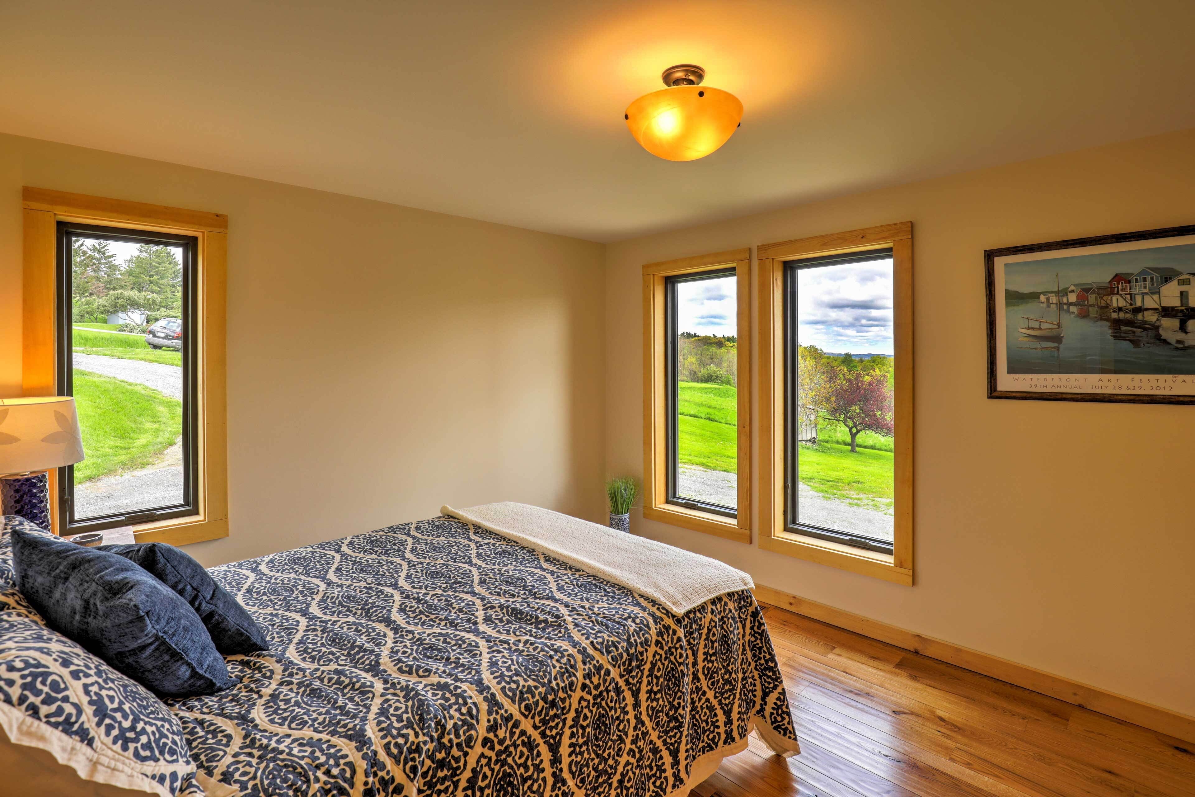 A bedroom with a bed, large windows, a ceiling light, and a framed picture on the wall.