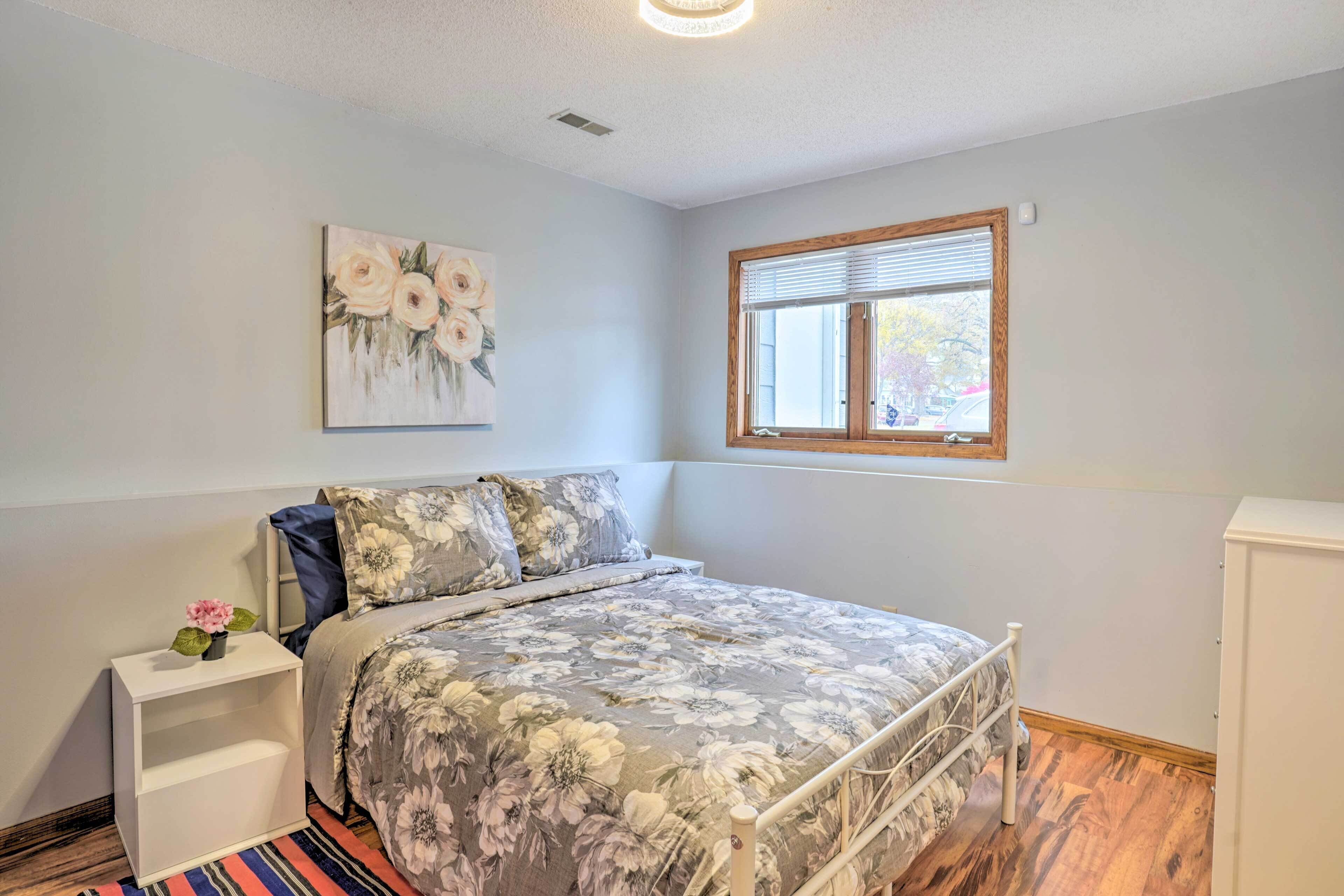 A bedroom with a bed, a nightstand, a painting, a window, and a cabinet.