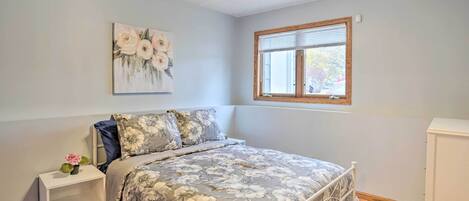 A bedroom with a bed, a nightstand, a painting, a window, and a cabinet.