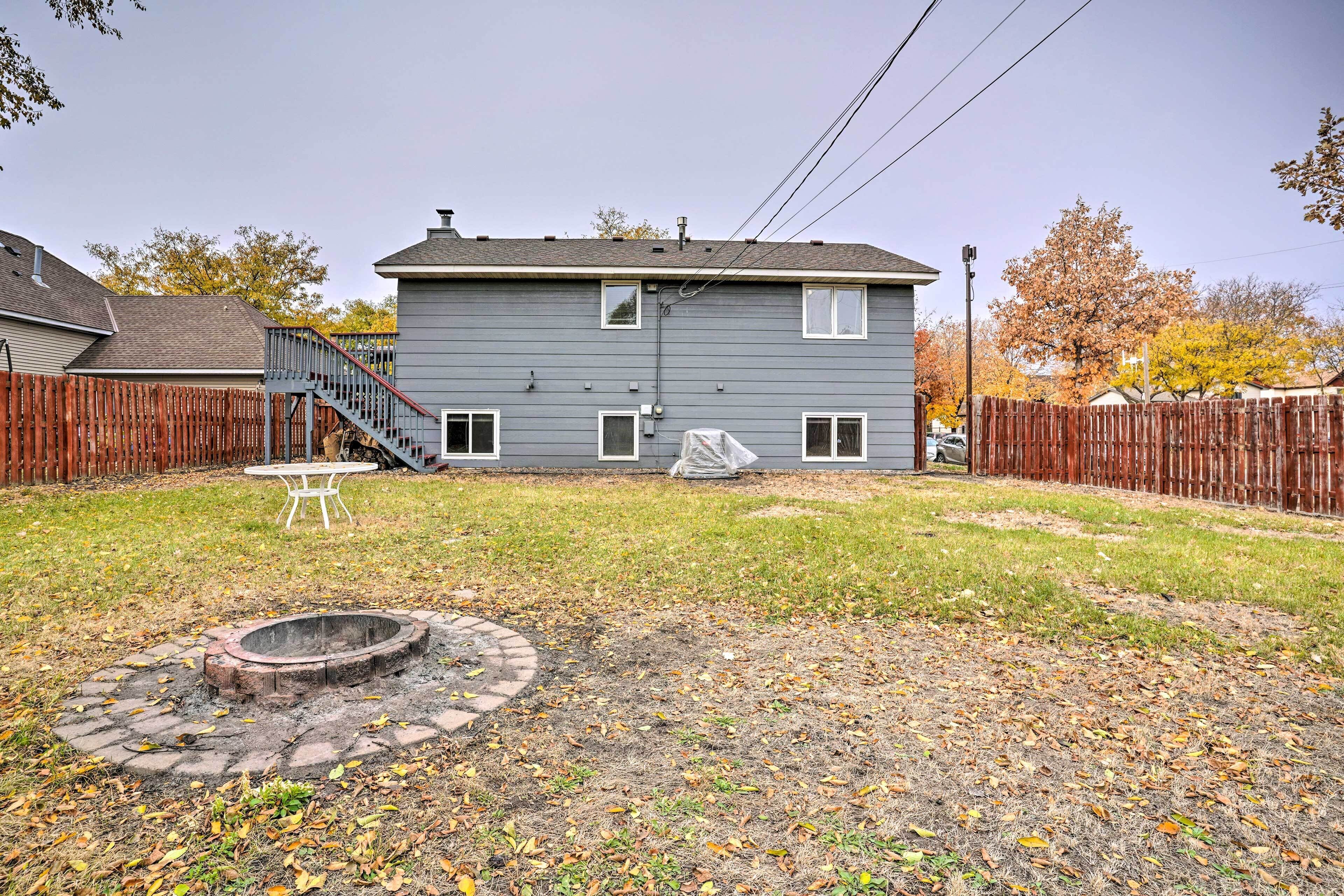 A two-story house with a fenced backyard, a fire pit, and a covered table.