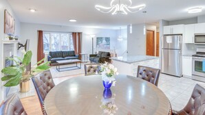 A modern kitchen with stainless steel appliances, a dining area with a round table and chairs, and a living room with a sofa and coffee table.