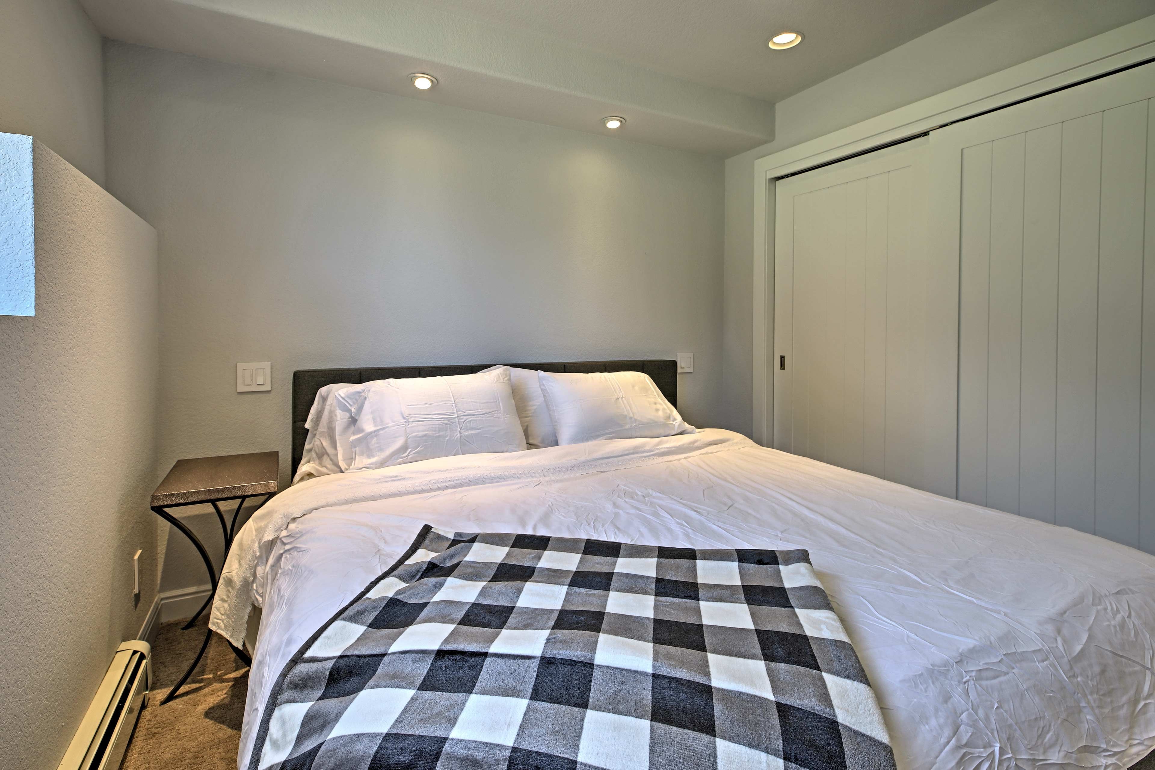 Una cama bien hecha con sábanas blancas, un plaid de cuadros y una mesita de noche con una lámpara.