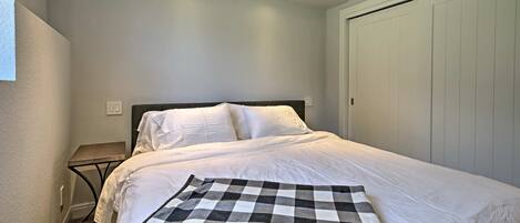 Una cama bien hecha con sábanas blancas, un plaid de cuadros y una mesita de noche con una lámpara.