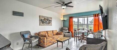 A living room with a sofa, chairs, a coffee table, a ceiling fan, and a dining area with a table and chairs.