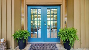 A blue door with glass panels, flanked by two potted plants, leading to an outdoor seating area. - Tranquil Mid-century Modern Cottage w/ Forest View (Cherokee Village)
