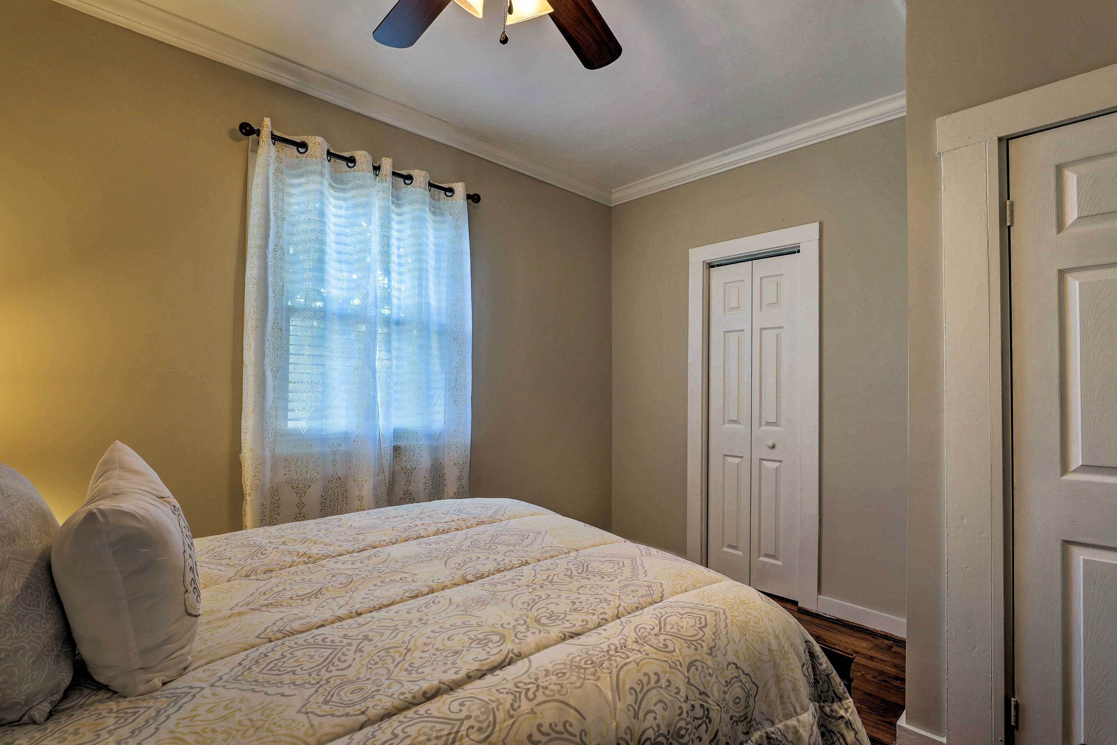 A bedroom with a bed, a ceiling fan, a door, and a window with curtains.