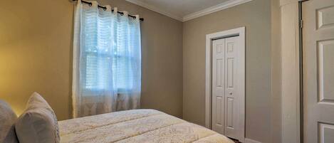 A bedroom with a bed, a ceiling fan, a door, and a window with curtains.
