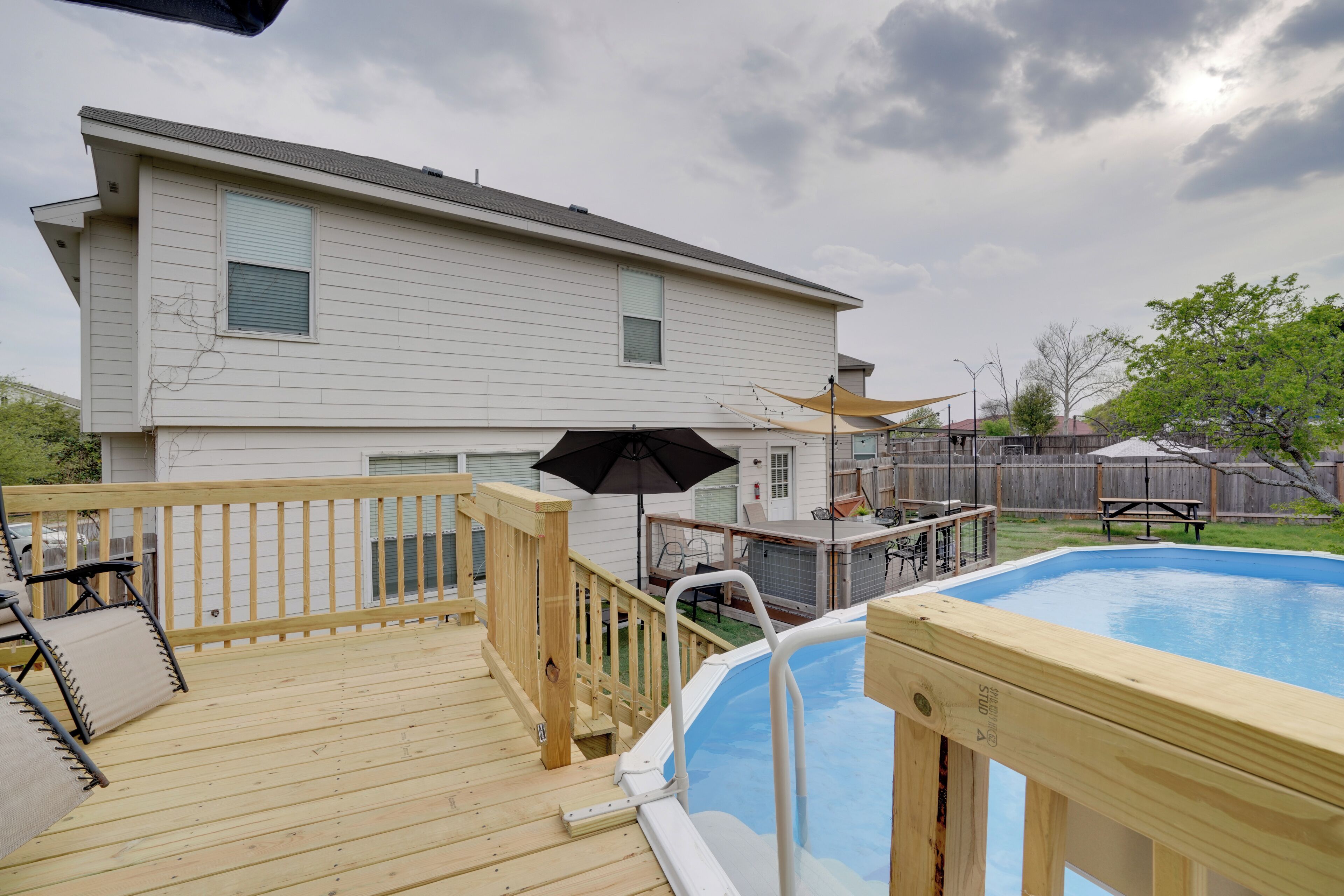 Un patio trasero con una terraza de madera, una piscina y una casa.