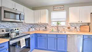 A kitchen with white cabinets, a blue countertop, stainless steel appliances, and a 'PANTRY' sign above the window.