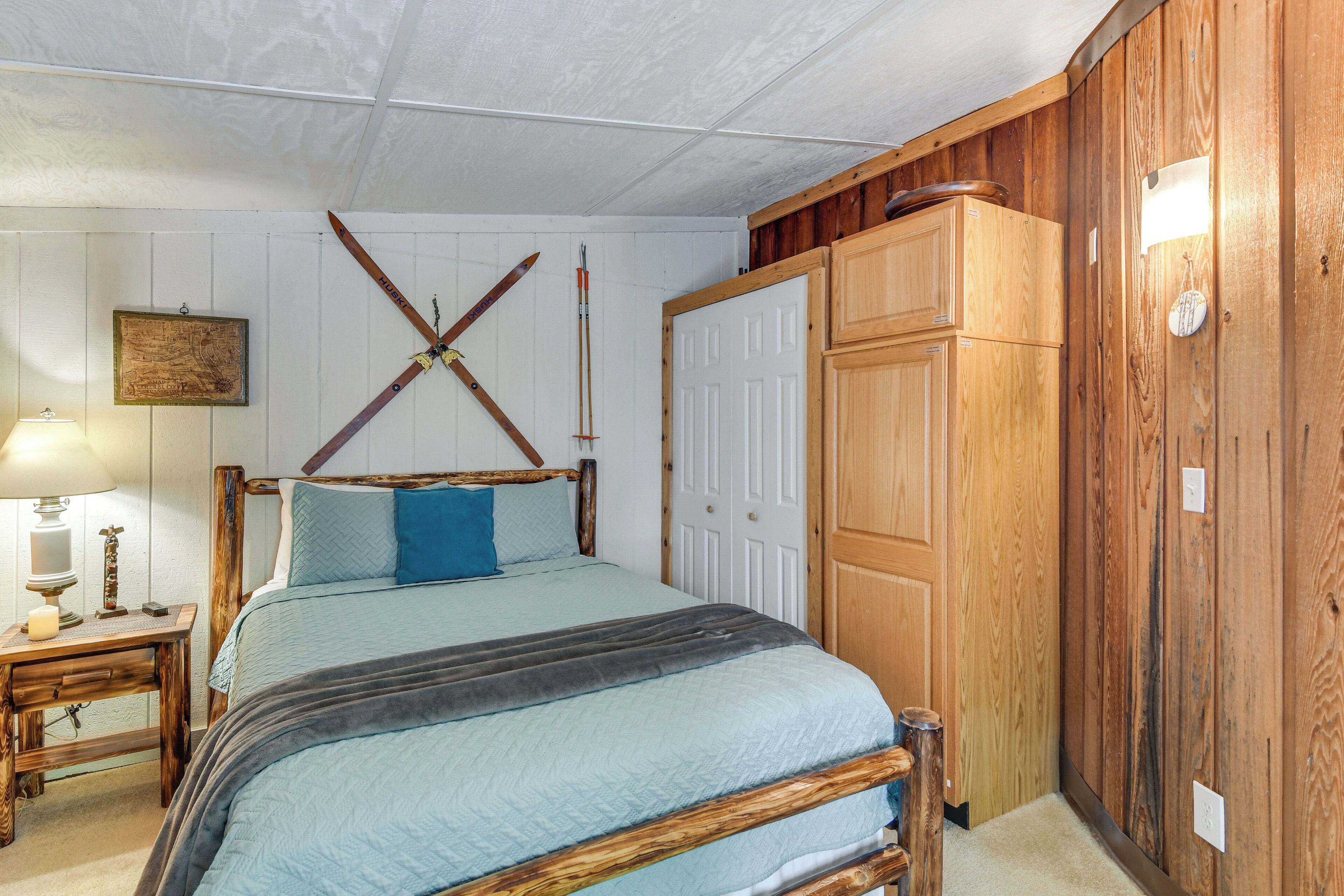 A bedroom with a wooden bed, a nightstand with a lamp, a wooden wardrobe, and a white door.
