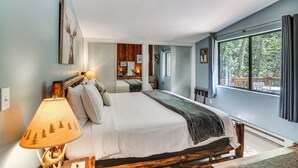 Une chambre avec un grand lit, une table de chevet avec une lampe, une fenêtre donnant sur des arbres et une tête de lit en bois.