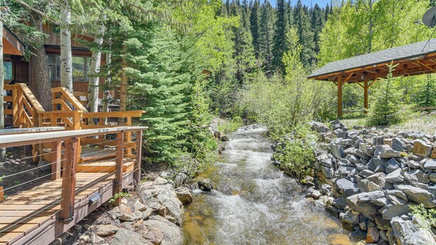 Un pont en bois enjambant un ruisseau, entouré d’arbres et d’une cabane.