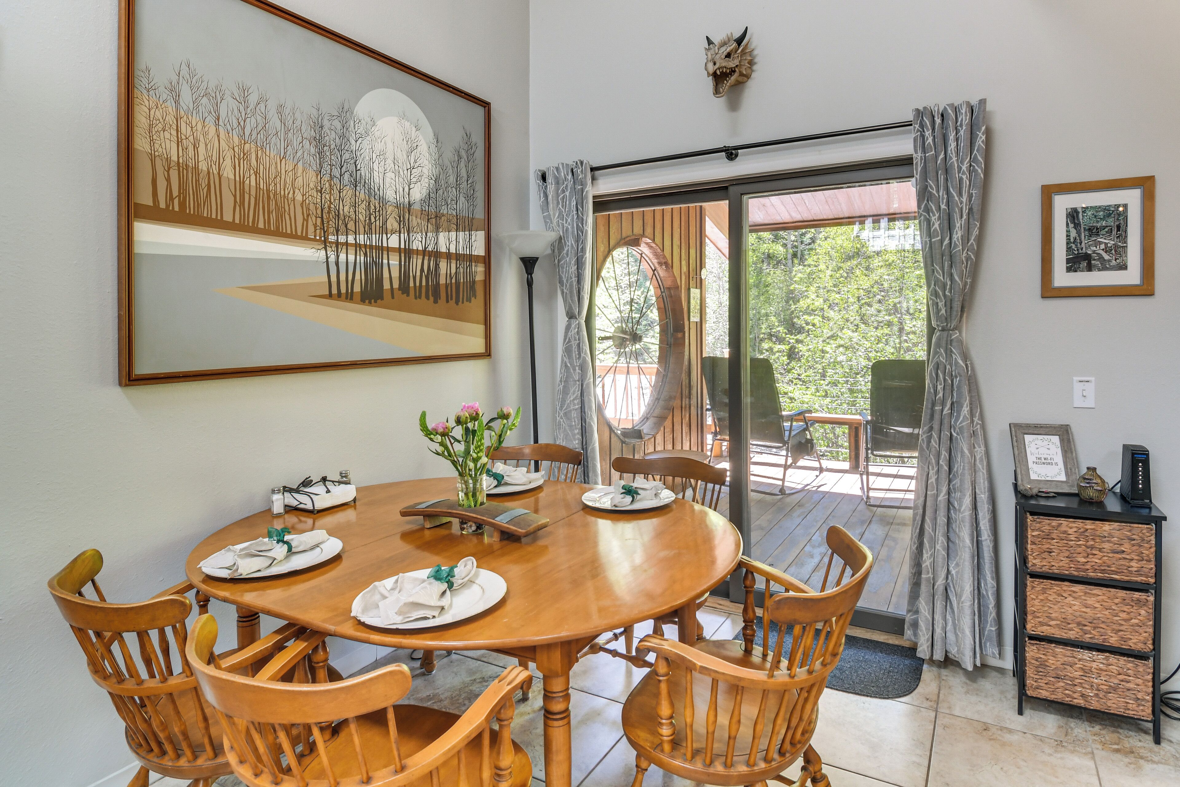 Un comedor con una mesa de madera preparada para cuatro, rodeada de sillas de madera. Un cuadro enmarcado está en la pared sobre la mesa.