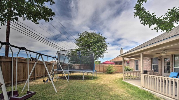 A backyard with a trampoline, wooden fence, and a covered patio area.