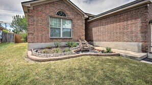 A brick house with a large window, a small garden with a wooden fence, and a concrete driveway.