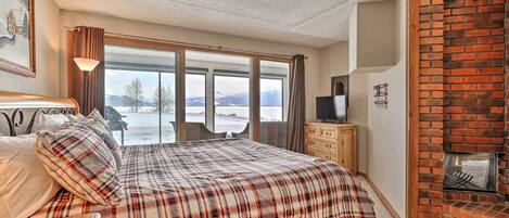 A bedroom with a large bed, a wooden dresser, a TV, and a brick fireplace.