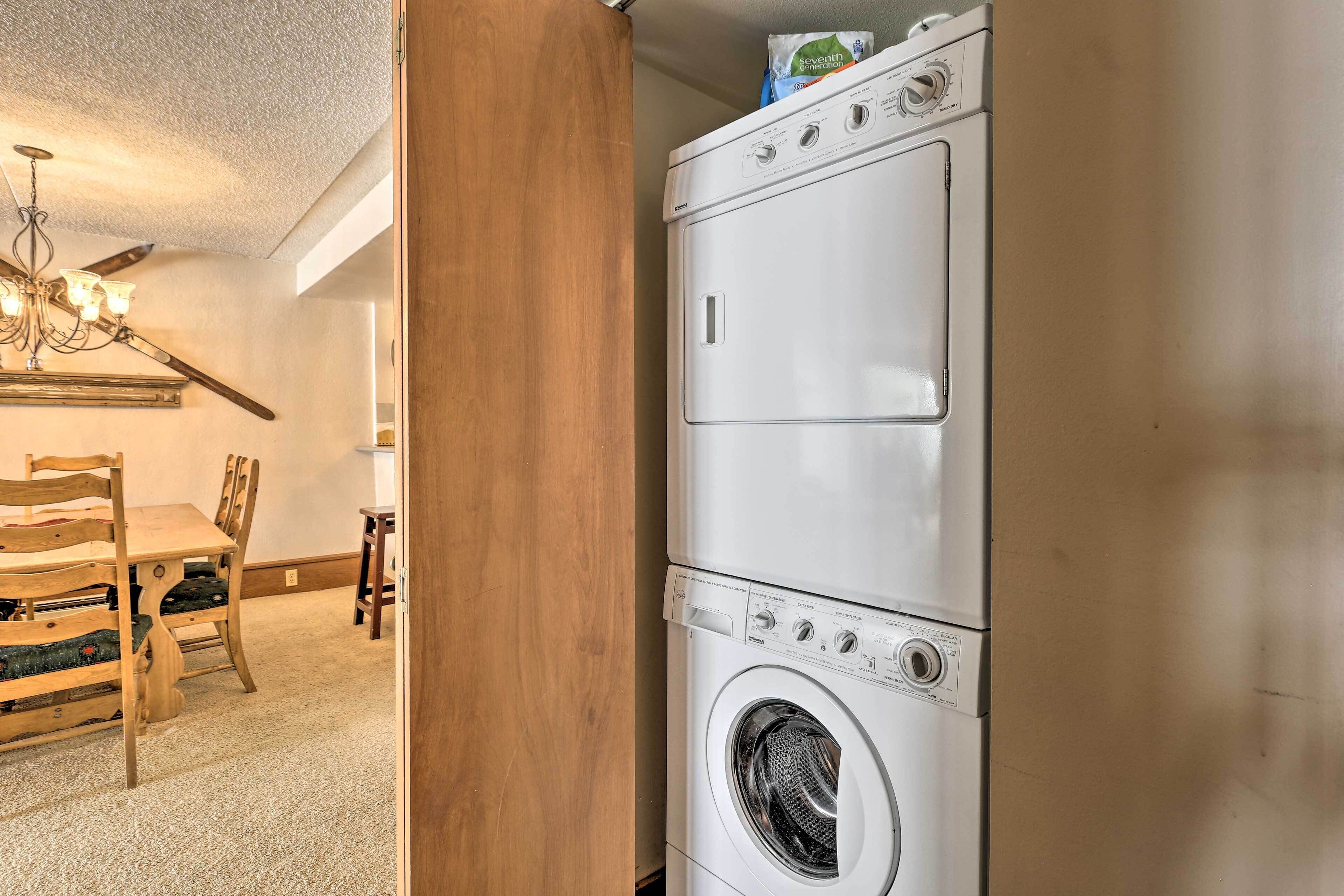 A laundry room with a stacked washer and dryer, wooden chairs, and a chandelier.