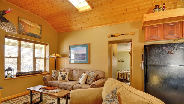 A cozy living room with a sectional sofa, a wooden ceiling, and a black refrigerator.