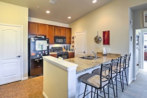 A kitchen with wooden cabinets, a black refrigerator, a microwave, a sink, and a granite countertop with bar stools. - 18 Mi to Winter Park: Granby Condo w/ Covered Deck (Granby)