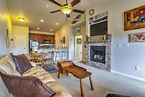 A living room with a sofa, coffee table, and fireplace. There is a kitchen in the background with a dining area. - 18 Mi to Winter Park: Granby Condo w/ Covered Deck (Granby)