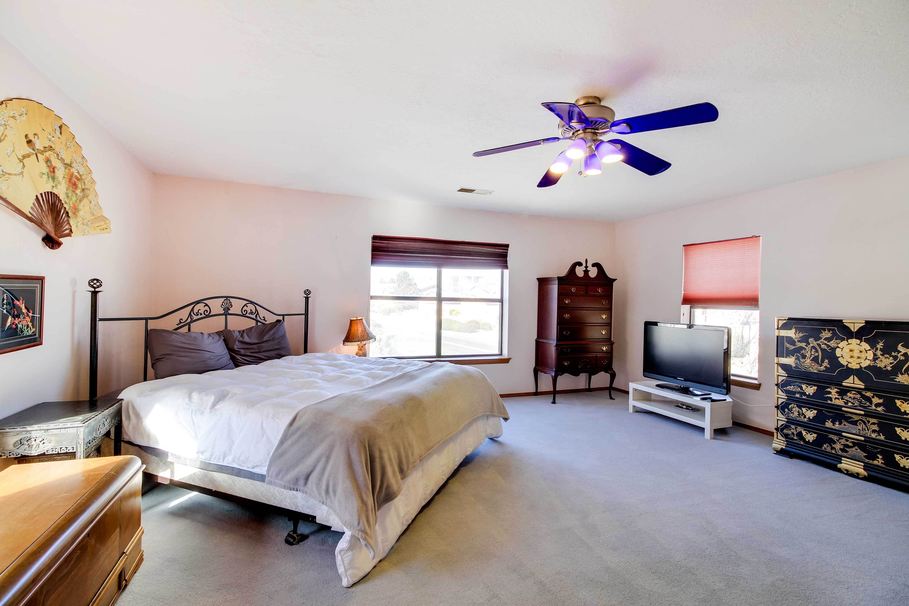 Un dormitorio con cama, televisión, cómoda, ventilador de techo y ventana.