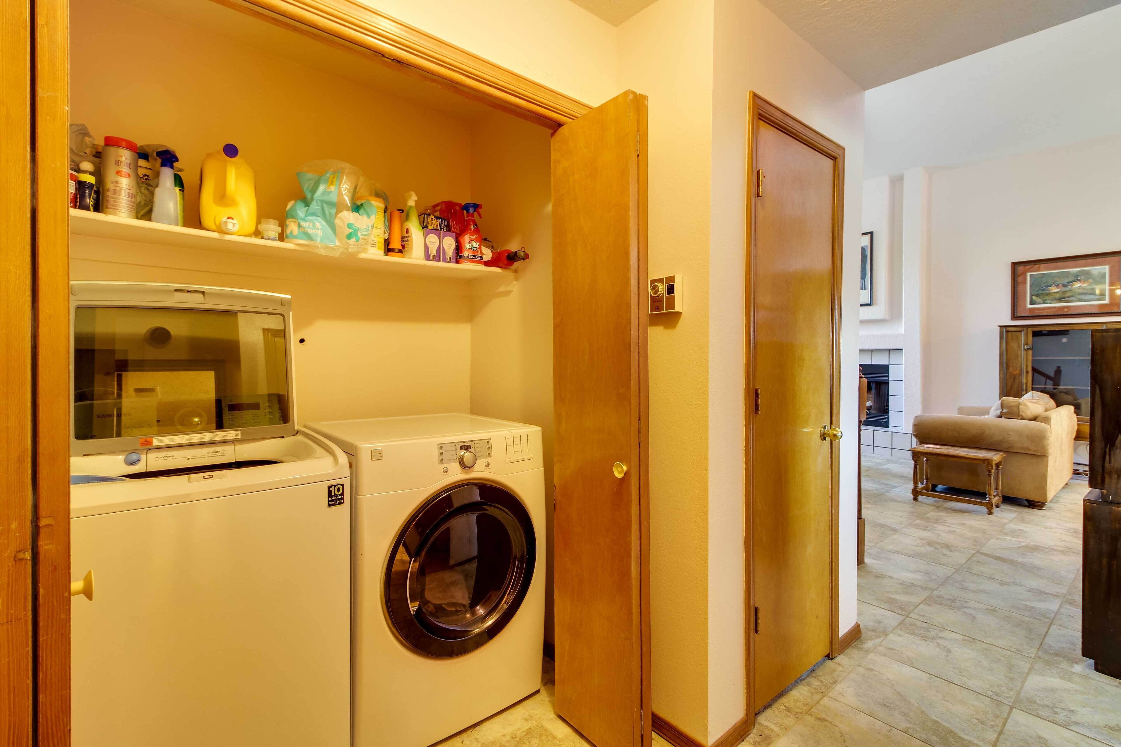 A laundry room with a washing machine and dryer, a shelf with cleaning supplies, and a wooden door.