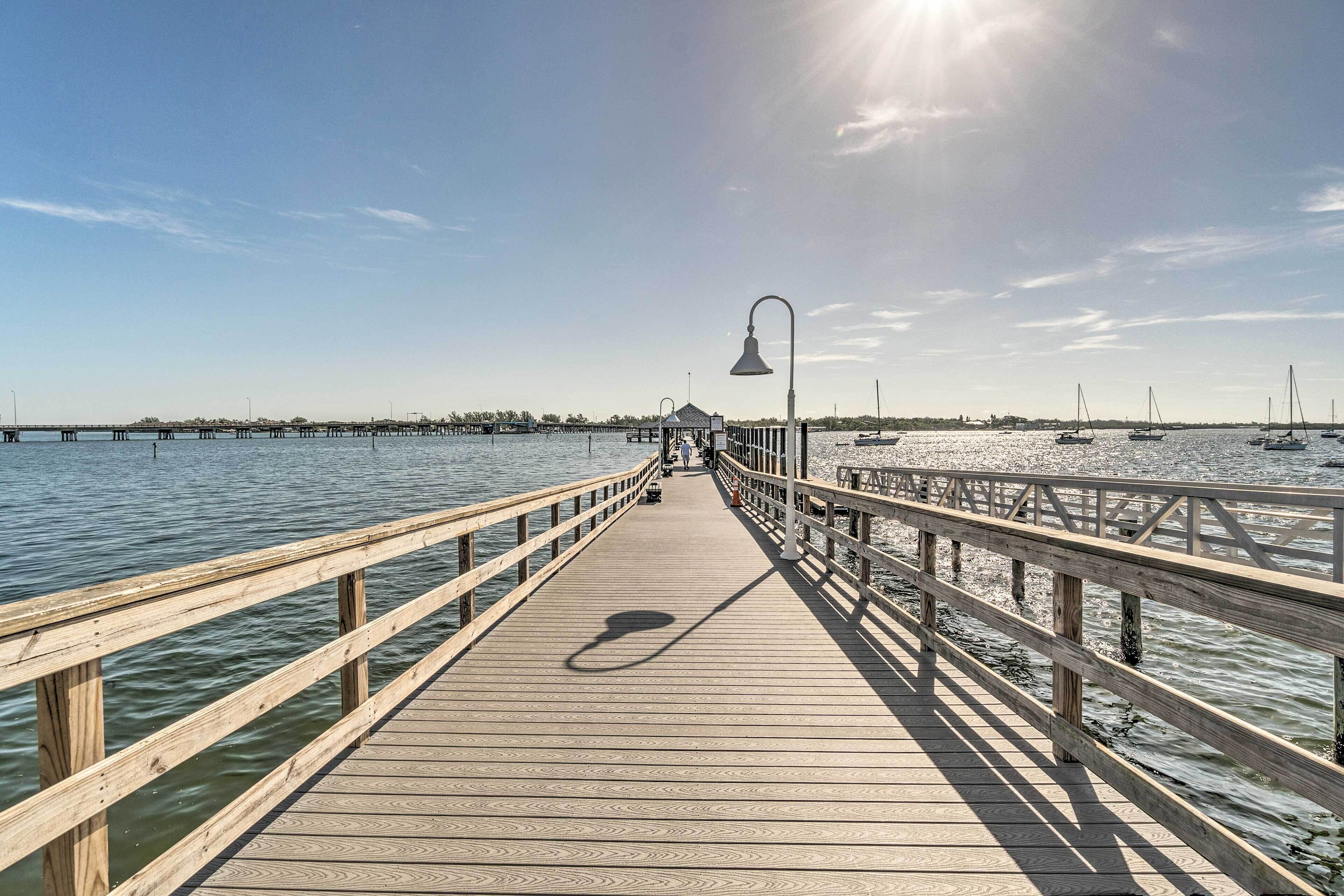 A wooden pier extending into calm waters with boats in the distance and a clear sky above.