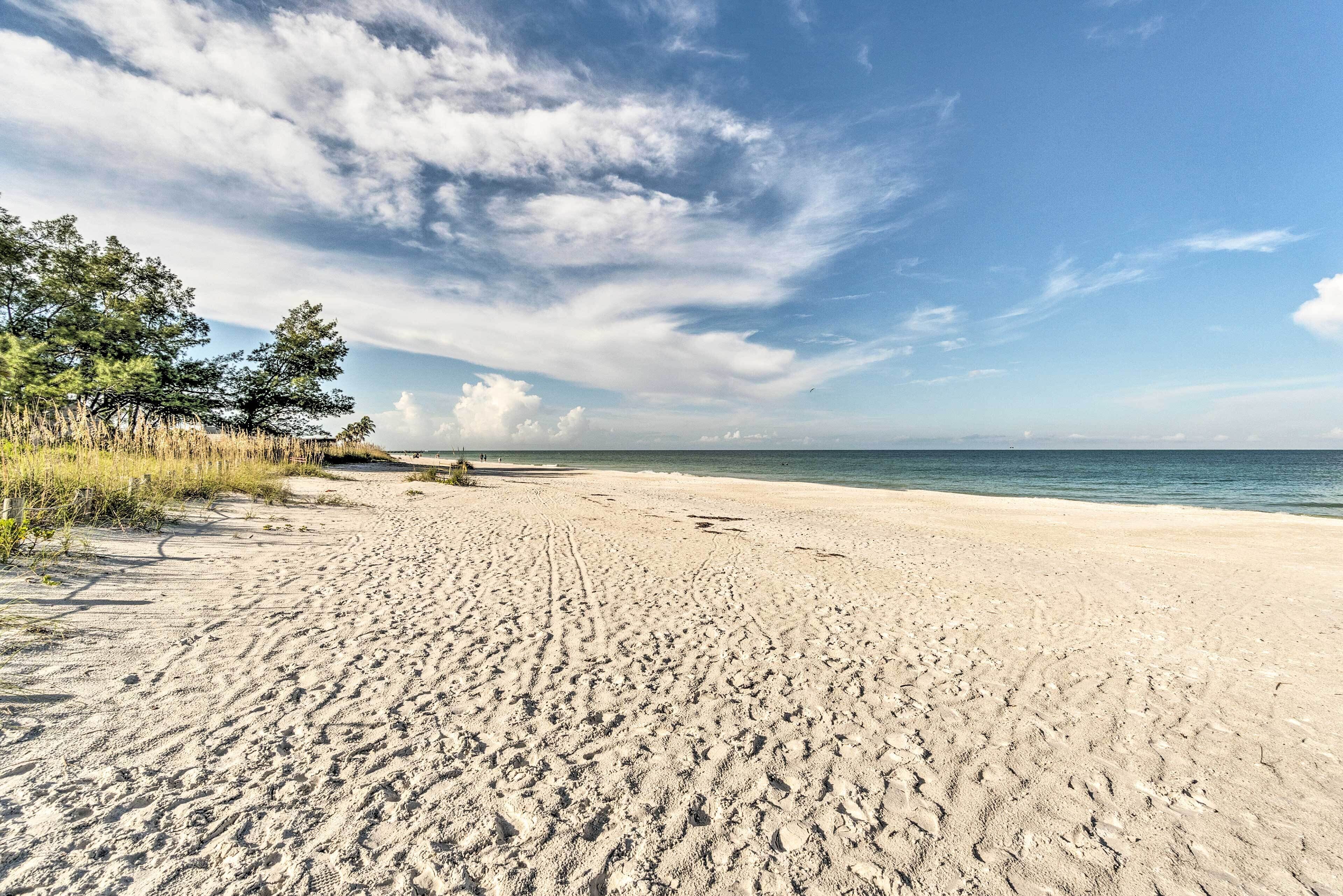 Uma praia arenosa com pegadas e vegetação rala.