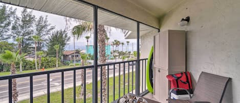 A balcony with a table holding a bowl of seashells, a chair, a red and black bag, and a blue container.