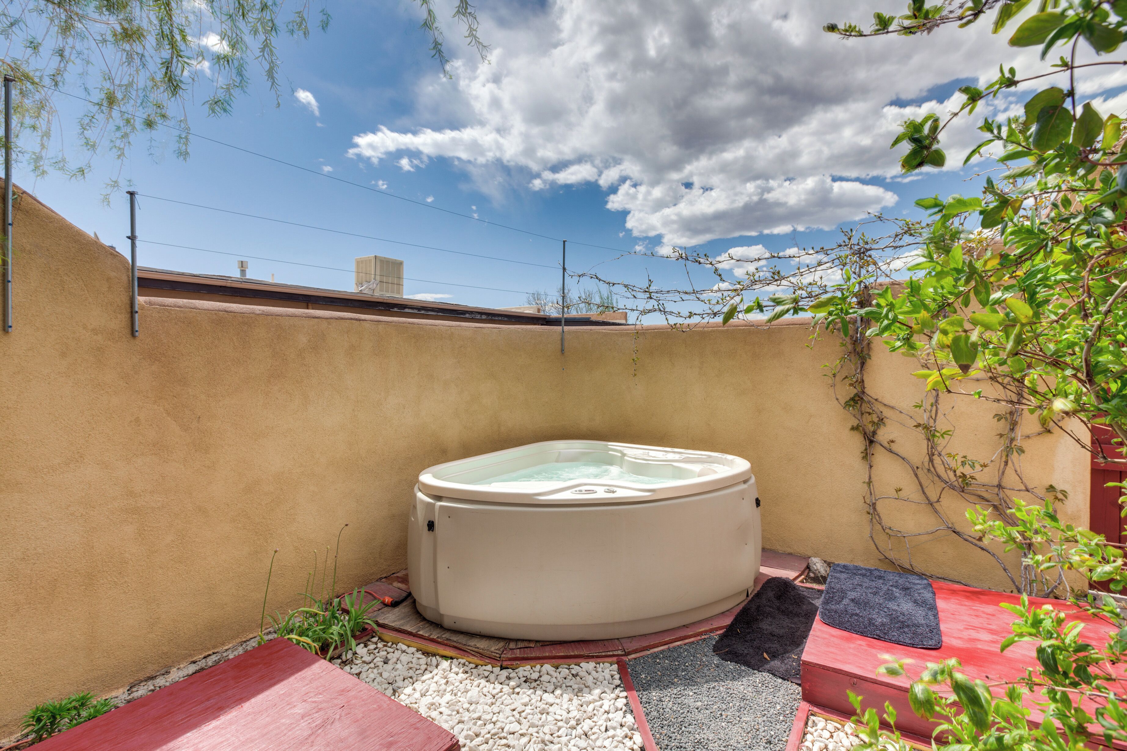 A hot tub in a courtyard with a beige wall, a red bench, and a black mat.